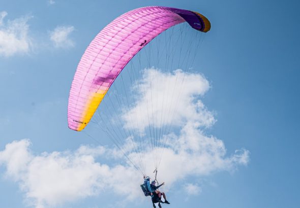 Experience the thrill of tandem paragliding with colorful parachute soaring high in the clear blue sky.