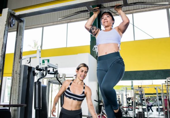 Two women practicing pull-ups in a modern indoor gym environment, emphasizing fitness and training.